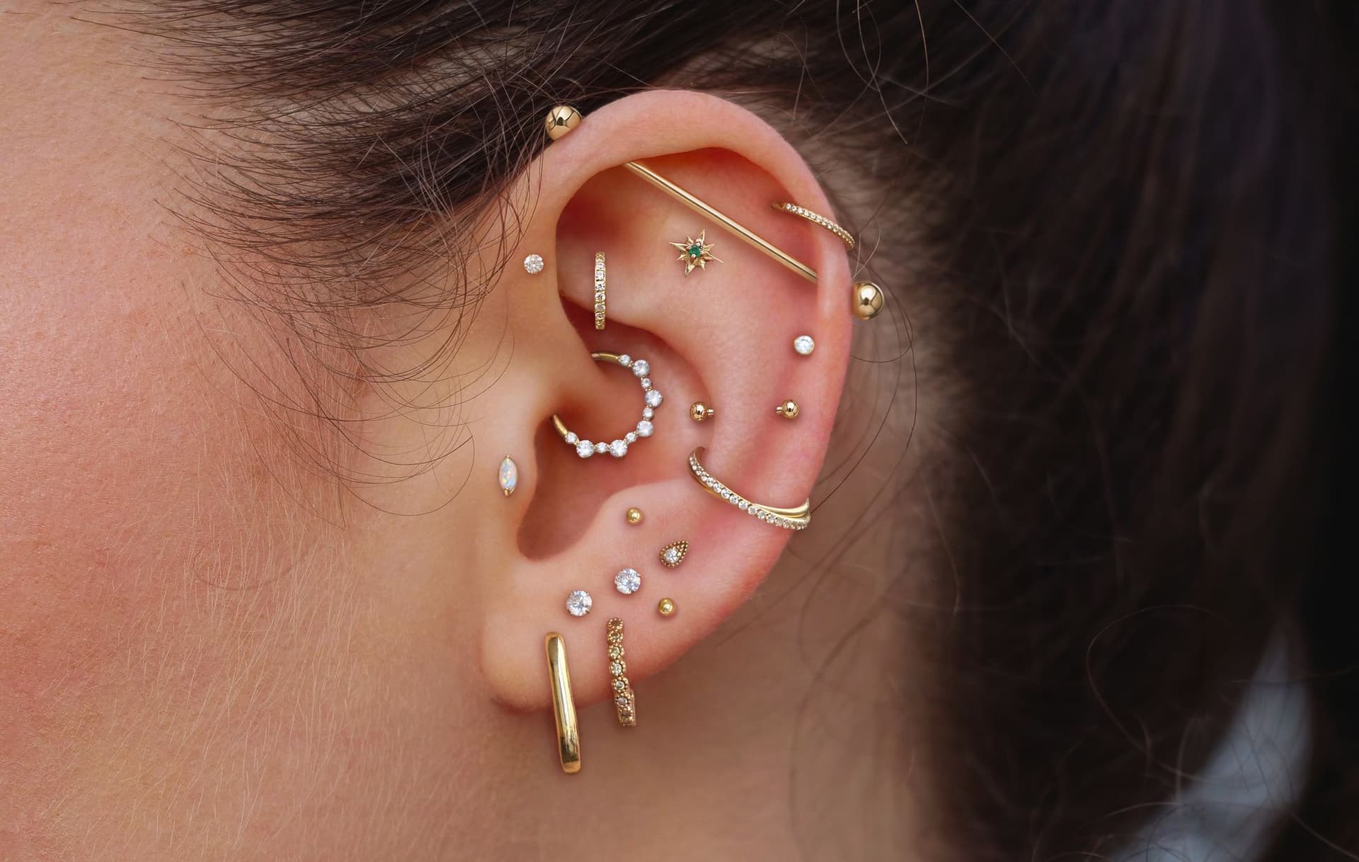 Oreille portant de nombreux piercings dorés : lobe, hélix, rook, daith, conch, tragus, industriel…
